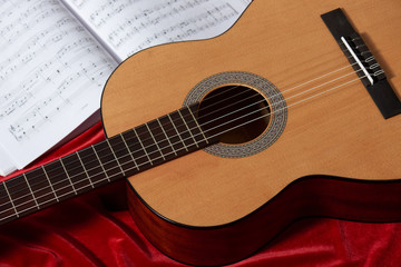 Obraz na płótnie Canvas acoustic guitar and music notes on red fabric, close view of objects