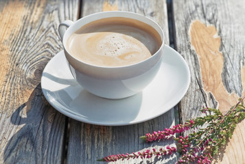 A cup of coffee and heather flowers on rustic wooden table