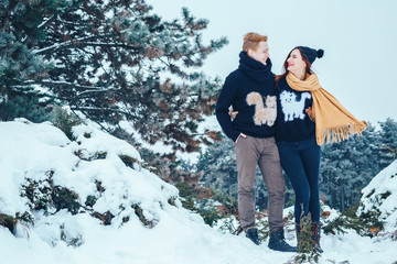 The guy and the girl have a rest in the winter woods. Husband and wife in the snow. Young couple walking in winter park.