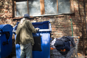 Poor old tramp in search for food or empty bottles. Way of life of old homeless man.