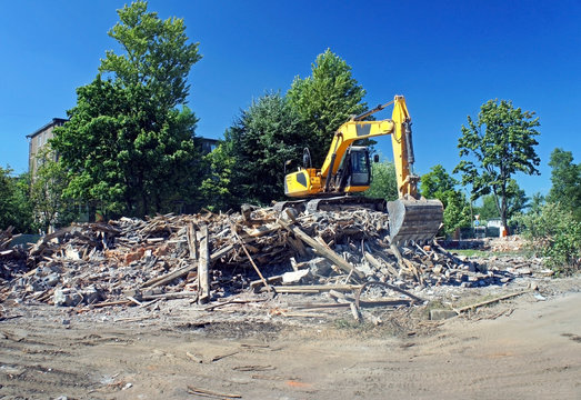 Excavator working at the demolition of an old house, yellow machine, construction site, sunny day