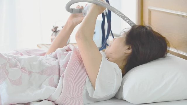 Senior woman unmasking after waking up in the morning  from continuous sleep without snoring and choking.Sleep apnea is a serious condition, wearing CPAP mask at night is the effective treatment .
