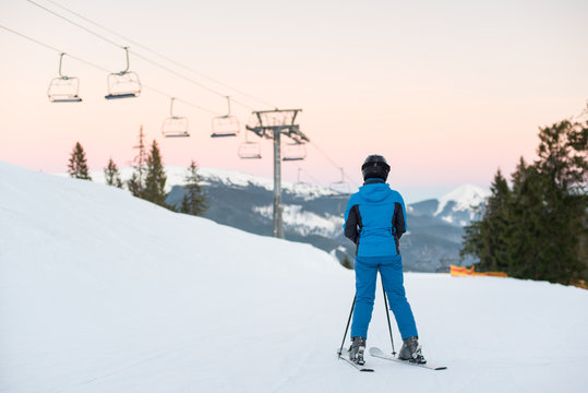 Woman skiers standing on snowy mountain enjoying beautiful mountain landscape on a winter resort at the background ski lifts and mountains. View of the back