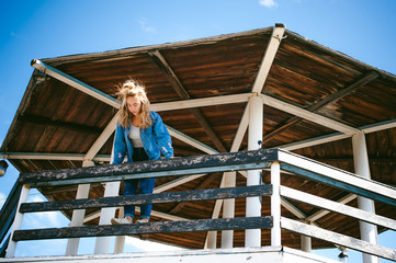 young beautiful woman in jeans clothes outdoors. portrait of a girl with freckles on her face, stylish girl on sea beach rescue tower, on a sunny summer autumn day.