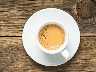 black frothy coffee in white cup with saucer on aged wooden background