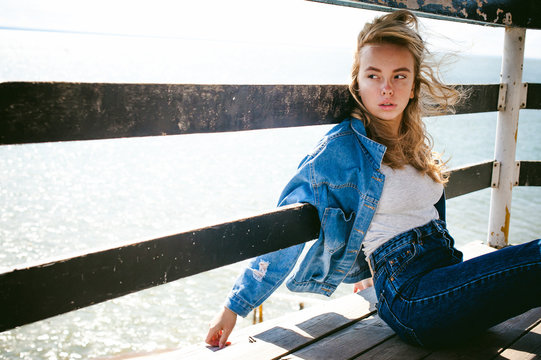 young beautiful woman in jeans clothes outdoors. portrait of a girl with freckles on her face, stylish girl on sea beach rescue tower, on a sunny summer autumn day.