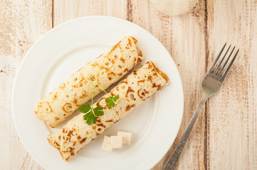 Food photography. Thin pancakes with filling and slices of cheese with herbs
