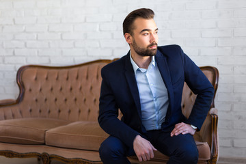 richness, success and fashion concept - handsome man in business suit sitting on vintage sofa