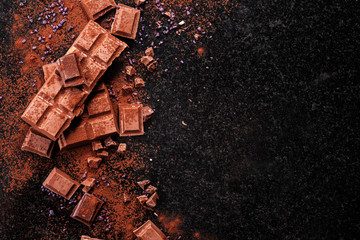 Broken chocolate pieces and cocoa powder on marble.