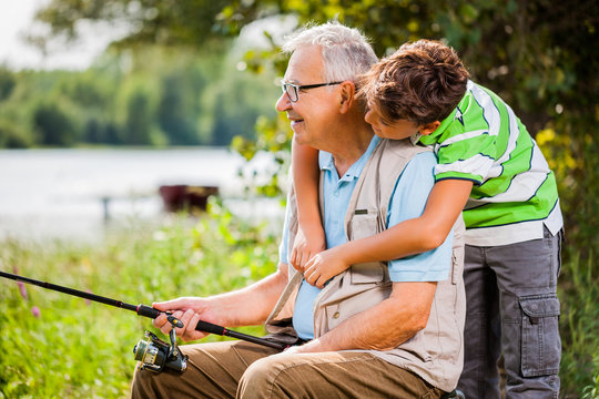 Grandfather and grandson are fishing on sunny day.