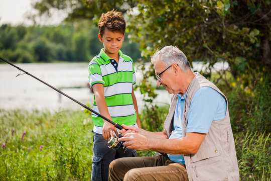 Grandfather and grandson are fishing on sunny day.