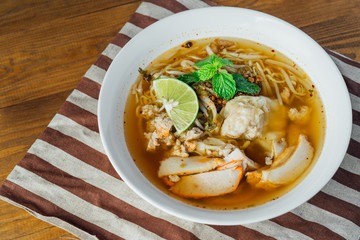 Noodle pork soup with Tom Yam spicy in white bowl on wooden table background.
