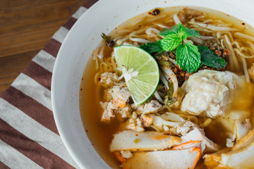 Noodle pork soup with Tom Yam spicy in white bowl on wooden table background.