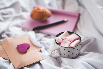 Cup of coffee in bed with love letters and open book with cake on background. Good morning. Selective focus.