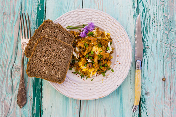 Delicious scrambled eggs with chanterelle mushrooms and chives on a wooden background. 
