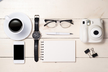Office desk. Pen, eyeglasses, coffee, camera, smartphone, watch and notebook on table. Top view.