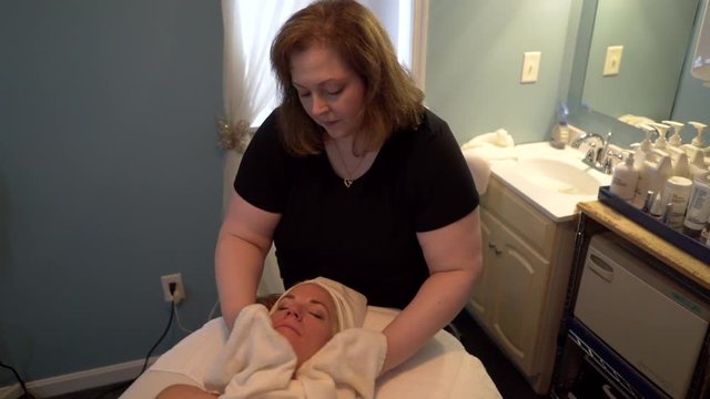 Massage therapist massages a beautiful mature woman’s face as part of her facial massage. Steadicam shot.