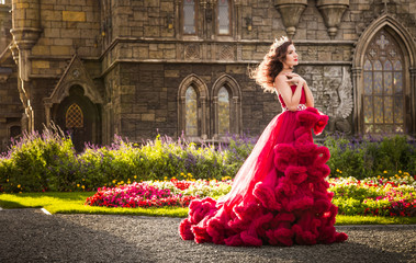 A beautiful woman, a queen in a burgundy lavish dress, walks along a flowering garden. Ancient,...