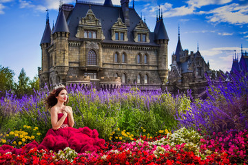 A beautiful woman, a princess in a red dress, sits by in a blooming garden. An ancient castle in...