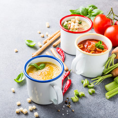 Assorted delicious homemade soups in enamel mugs with ingredients. Healthy food concept.