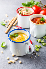Assorted delicious homemade soups in enamel mugs with ingredients. Healthy food concept.