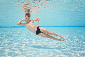 Happy small boy swim underwater, has fun and dive in the blue transparent water of clear pool. Swimming classes and water safety education. Family vacation, weekend with kids