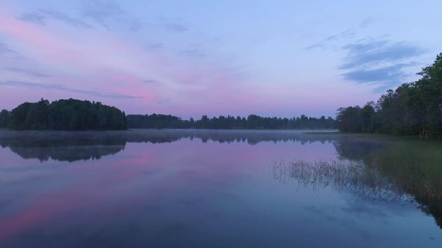 Aerial drone shot flying low over a misty and calm lake before dawn