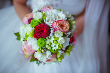 Rich wedding bouquet of roses, peonies and greenery in bride's arms
