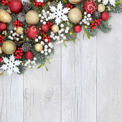 Fototapeta na wymiar Christmas background with bauble decorations, holly, mistletoe, ivy, fir and pine cones on rustic white wood background.