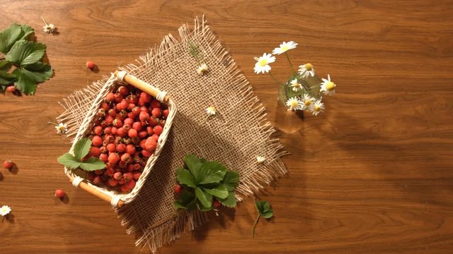Strawberries on the table. Top view.

The smooth glide of the camera ( from left to right ) over the table on which there is a basket of strawberries and chamomile in a glass.