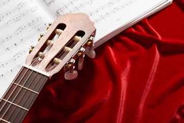 acoustic guitar and music notes on red velvet fabric, close view of objects