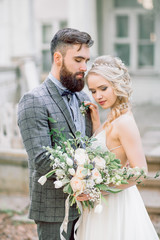 Handsome bearded groom hugging pretty blonde bride.