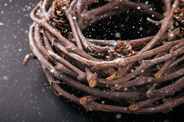 Christmas Wood Wreath with Natural Twigs and Cones.Festive decoration on a Black Background.Vintage style.Drawn Snowfall. selective focus.
