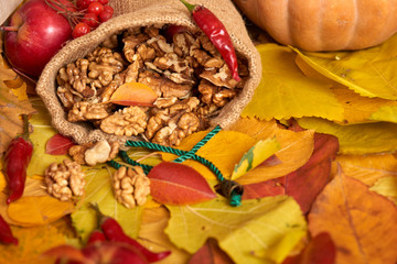 Nuts in a sack, fruits and vegetables on fallen leaves background, autumn season