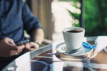 cup of coffee on a table in a cafe and men's hands with a phone in a blurry background