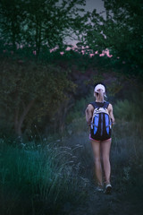 Lonely young girl hiker with backpack walks in forest in the evening