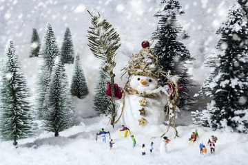 Snowman and miniature people in pine woods during winter