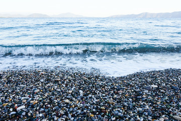 Fototapeta na wymiar Sunrise, morning over sea with foamy waves against pebbles on a beach, coast
