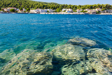 Rocky shallows with crystal clear water and beautiful settlement over blue sea - obrazy, fototapety, plakaty
