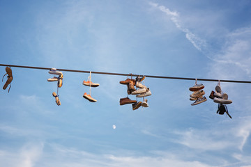 Shoes hanging on an electric cable against a blue sky and moon.
