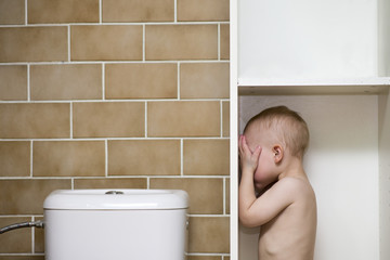Boy standing in a bathroom cabinet covering his eyes with his hands with space for text or picture...
