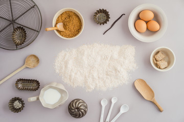 Flatlay collection of tools and ingredients for home baking on light grey background with flour...