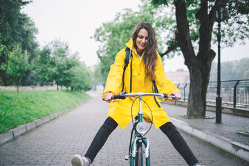 Cheerful young woman riding bicycle and wearing raincoat