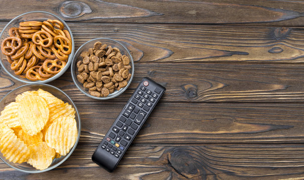 TV Remote control, snack chips, on a wooden background top view space for text. layout.
