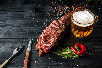 Barbecue dry aged rib of beef with spice, vegetables and a glass of light beer close-up on black...
