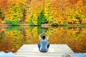 Woman meditating outdoors in the autumn park near forest lake.