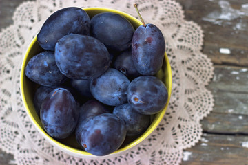 Top view of plums in yellow bowl, on wooden background
