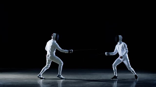 Two Professional Fully Equipped Fencers Expertly Fight with Foils. One Performs quick Lunge Attack. Shot in Slow Motion and on Isolated Black Background. 