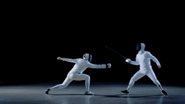 Two Professional Fully Equipped Fencers Expertly Fight with Foils. One Performs quick Lunge Attack. Shot in Slow Motion and on Isolated Black Background. 