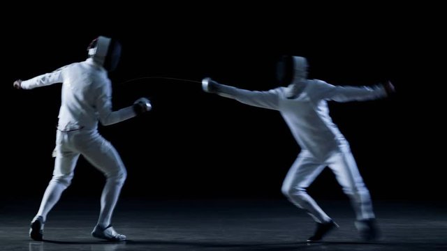 Two Professional Fencers Show Masterful Swordsmanship in their Foil Fight. One Performs Beautiful Fleche Attack. Shot Isolated on Black Background .